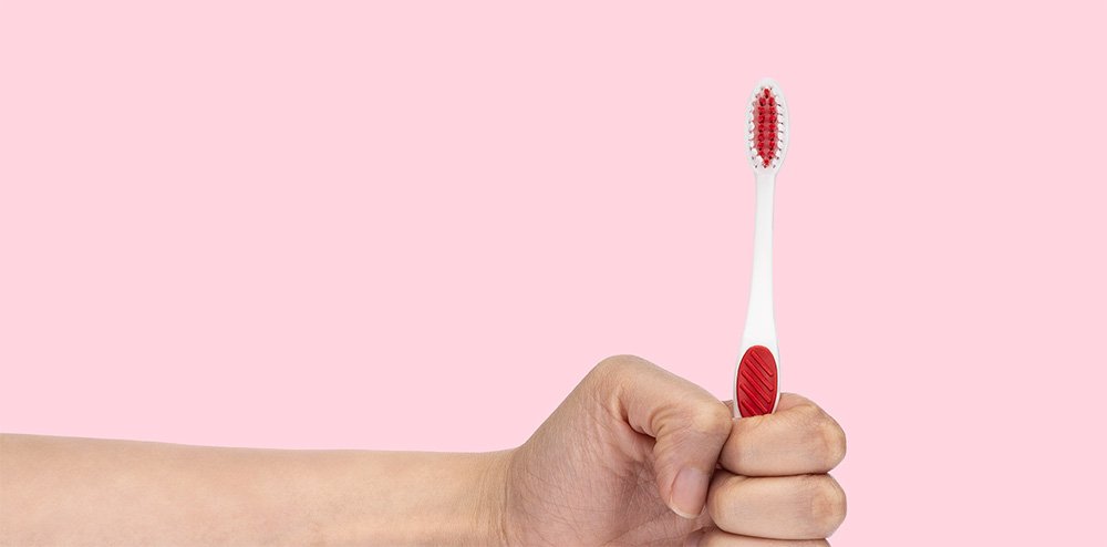 Made in the USA toothbrush being held on a pink background