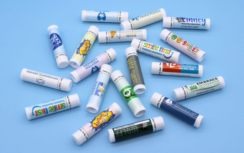 Scattered lip balms with various personalized logos from dental offices.